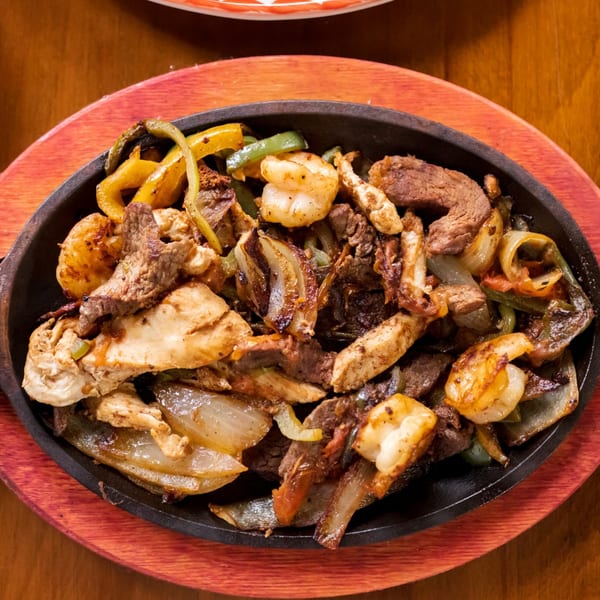 Sizzling fajitas with chicken, steak, shrimp, onions, and bell peppers in a black skillet.