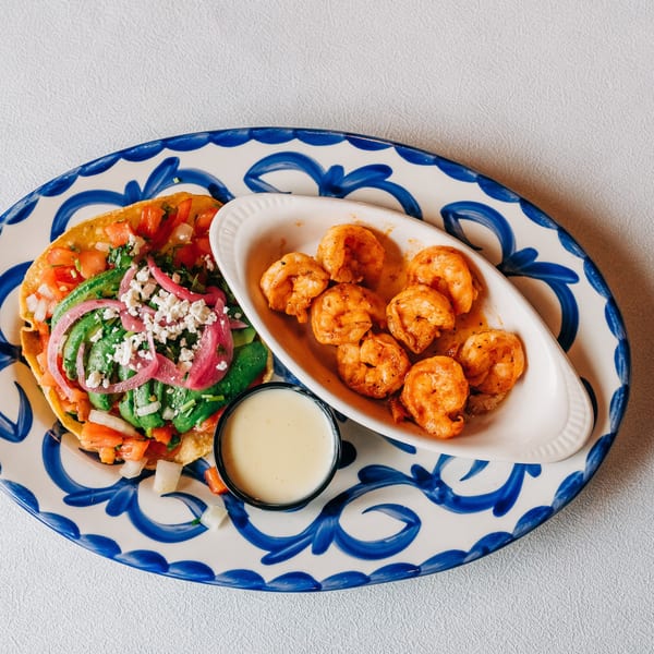 A Si Señor Taqueria tostada with avocado, pico, and cheese, served with seasoned shrimp and sauce.