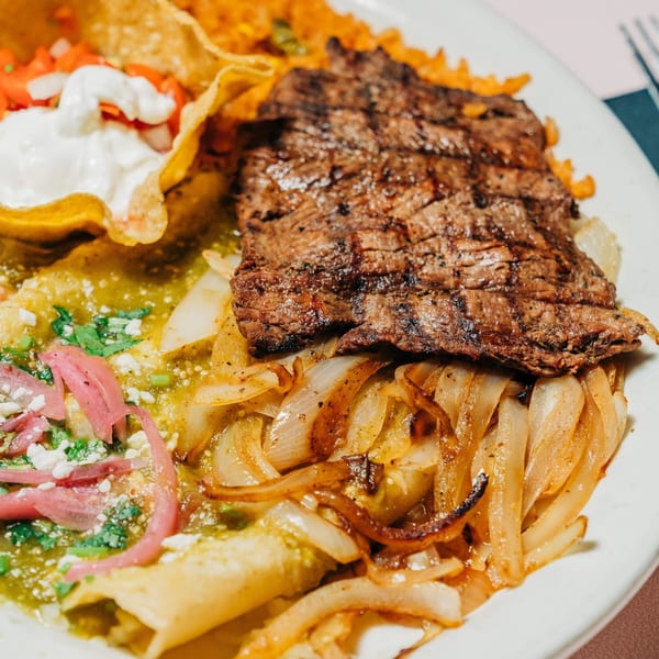 Grilled steak with caramelized onions, green enchiladas, rice, and tortilla chips with sour cream.