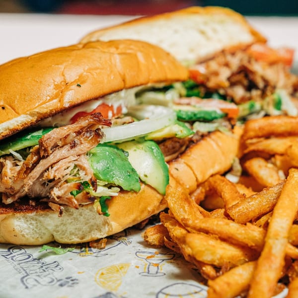 Two Mexican tortas with shredded meat, avocado, and onions, served with a side of fries.