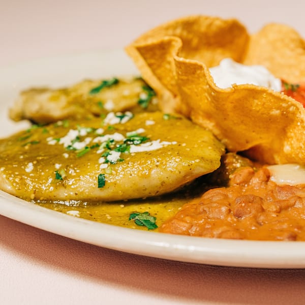 Si Señor Taqueria's enchiladas with green sauce, refried beans, and a crispy tortilla bowl with sour cream.
